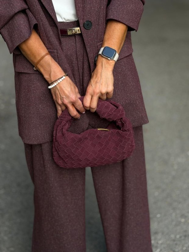 Bordová mini prepletaná kabelka Lesi z brúsenej kože v ruke, kombinovaná s elegantným bordovým outfitom.