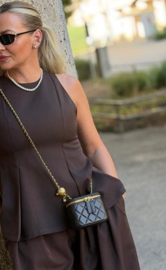 Tmavohnedá kožená kabelka Mini Aria s prešívaným dizajnom a zlatou retiazkou na elegantnom hnedom outfite.