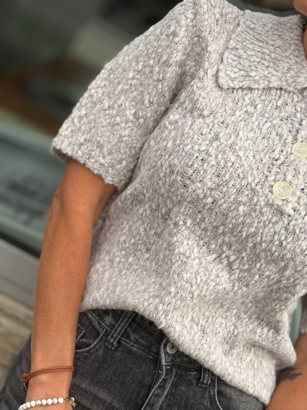 Sivý pletený sveter Giulia s krátkym rukávom, golierikom a gombíkmi na modelke.