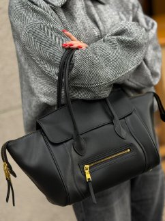 Čierna kožená kabelka Eline s dlhšími rúčkami, predným zipsovým vreckom a zlatým kovaním na modelke.
