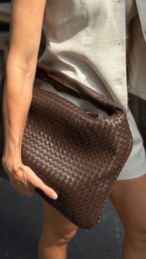Tmavohnedá prepletená maxi kabelka z pravej kože držaná v ruke pri ľanovom outfite