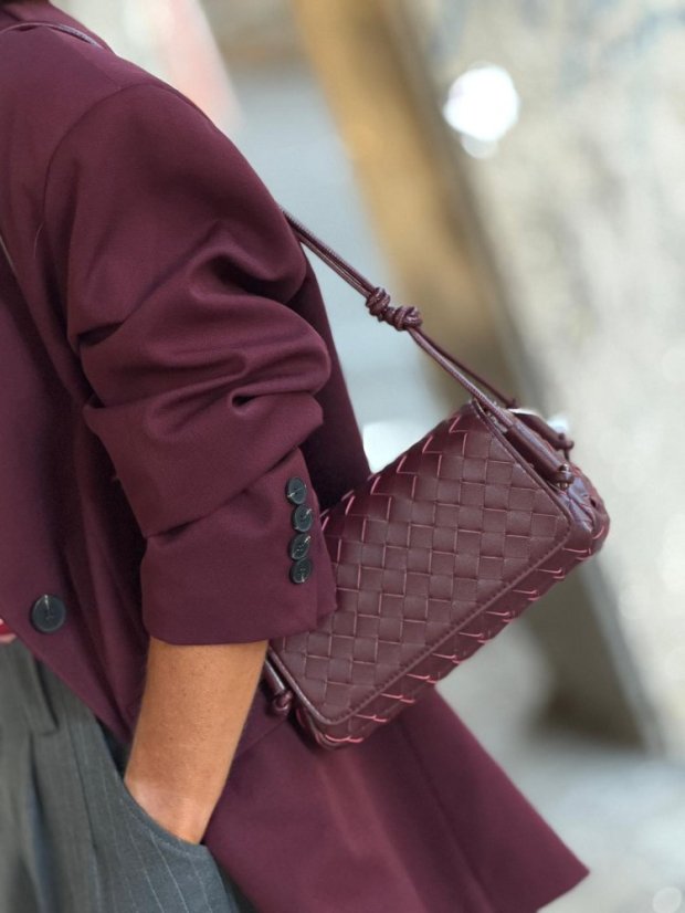 Prepletaná kožená kabelka Rena Burgundy v burgundy farbe na ramene modelky.
