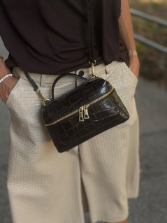 Hnedá kožená kabelka Mia Chocolate s lesklým croco efektom a zlatým zipsom na modelke.       Sources