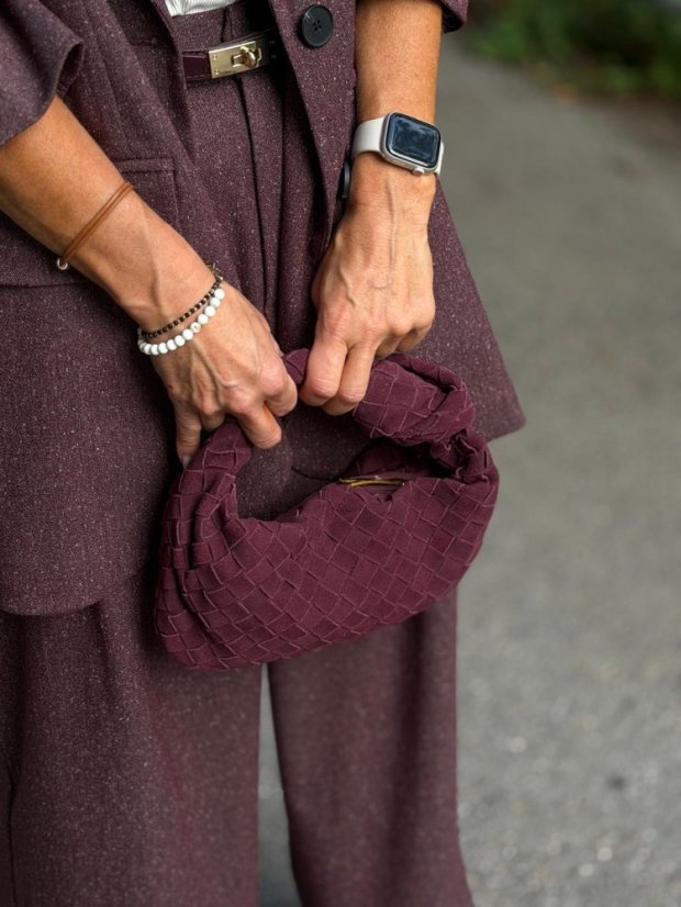 Bordová mini prepletaná kabelka Lesi z brúsenej kože v ruke, kombinovaná s elegantným bordovým outfitom.