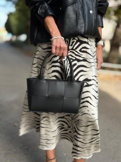 Elegantná čierna kožená kabelka s prepletaným dizajnom v ruke modelky.