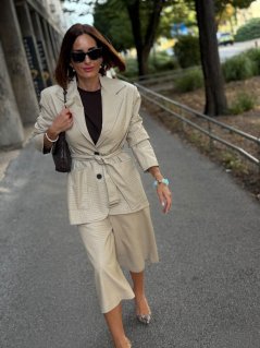 Béžové koženkové sako Atelier s opaskom v páse, jemnou štruktúrou materiálu a elegantným predĺženým strihom na modelke.