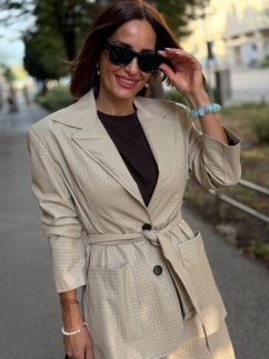 Béžové koženkové sako Atelier s opaskom v páse, jemnou štruktúrou materiálu a elegantným predĺženým strihom na modelke.