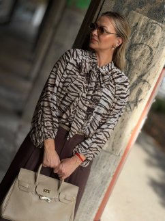 Hnedá blúzka Zebrano so zvieracím vzorom a viazaním pri krku na modelke. Hnedá blúzka Zebrano so zvieracím vzorom a viazaním pri krku na modelke.