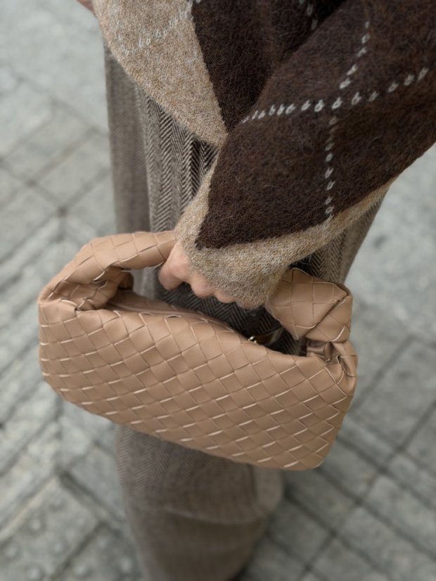 Béžová prepletaná kožená kabelka do ruky s elegantným tvarom.