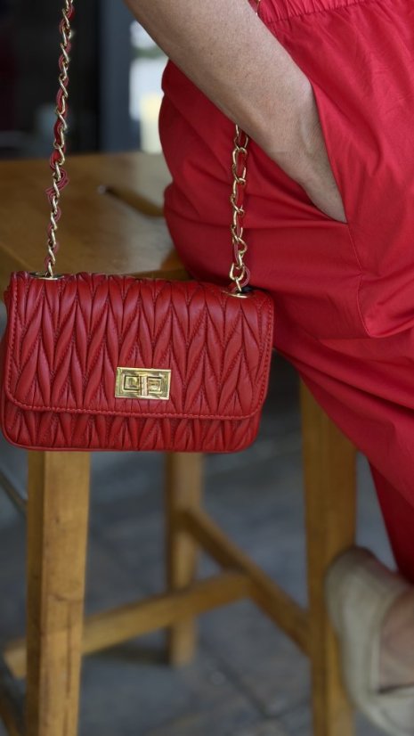 červená kožená mini kabelka so zlatou reťazou a prešívaným povrchom v rukách ženy